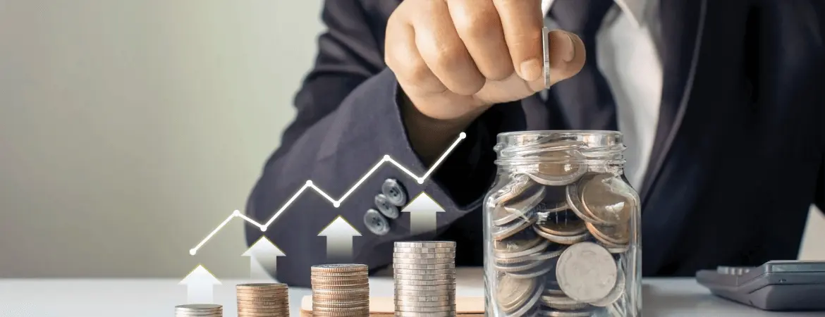 Businessperson stacking coins beside a jar of savings with an upward financial growth graph.